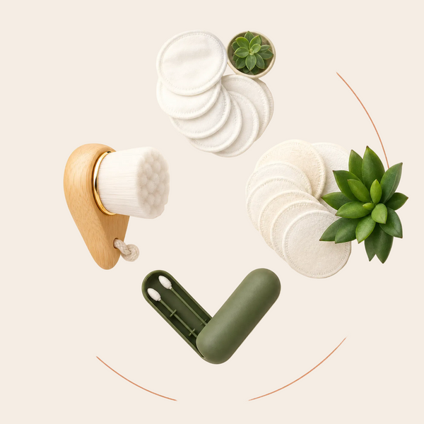 A flat-lay product shot of a skincare set on a warm beige background. The set includes a wooden-handled cotton swabber brush, a stack of white cotton pads, a green storage case, and two small potted succulent plants.
